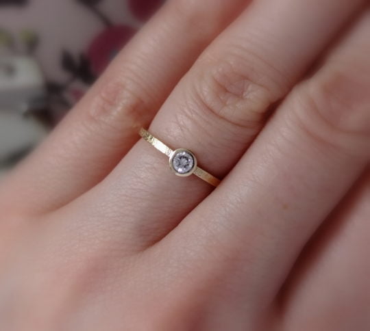 minimalistyczny złoty pierścionek z brylantem na palcu