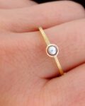 minimalistyczny złoty pierścionek z perłą i fakturowanym złotem na palcu