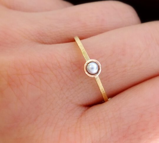 minimalistyczny złoty pierścionek z perłą i fakturowanym złotem na palcu