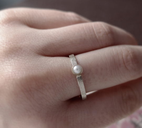 minimalistyczny złoty pierścionek z perłą z białego złota na palcu