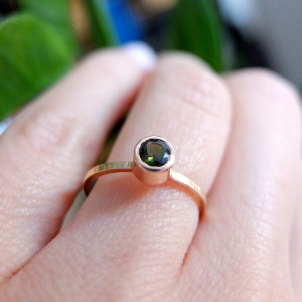 złoty pierścionek z zielonym turmalinem na palcu